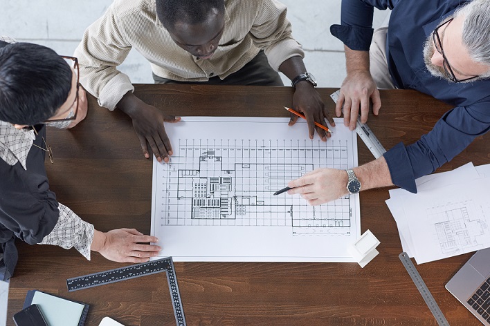 High angle view of blueprint on the table with engineers examining it and discussing in team at office